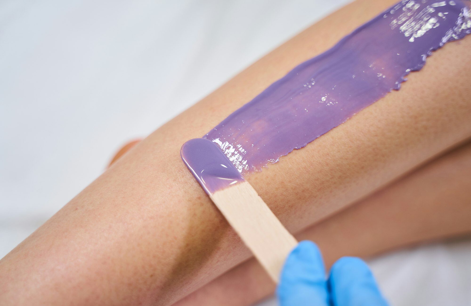 Professional beautician putting wax on female leg